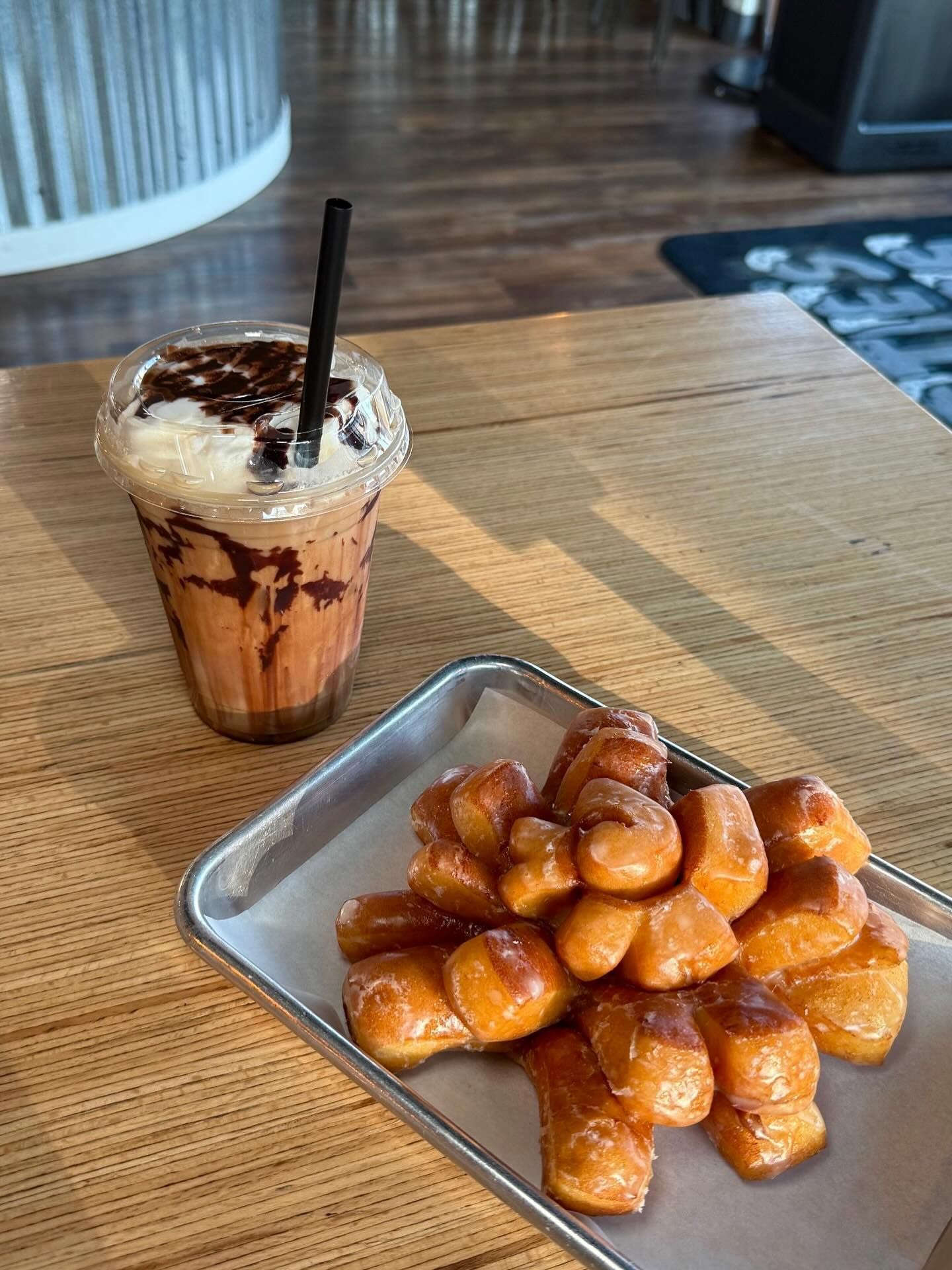 Iced coffee drink and a tray of glazed donut twists on a wooden table.