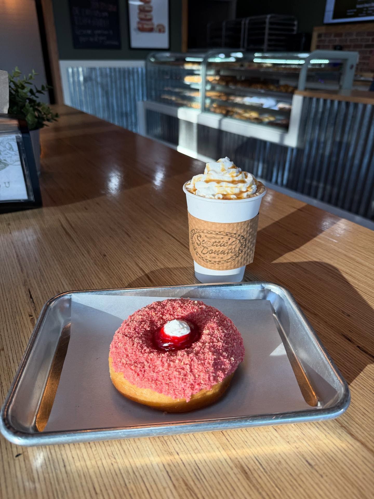 Donut with pink frosting and a coffee drink with whipped cream on a table in a cafe setting.