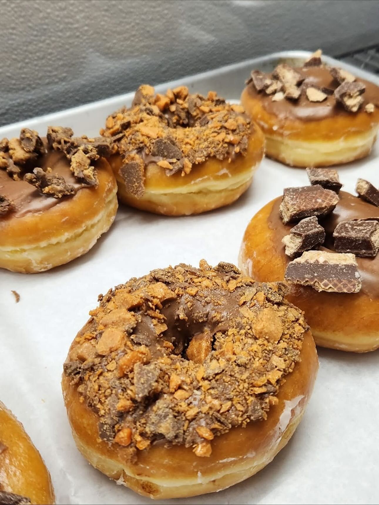 Glazed donuts topped with chocolate icing and peanut butter cup chunks on a tray.