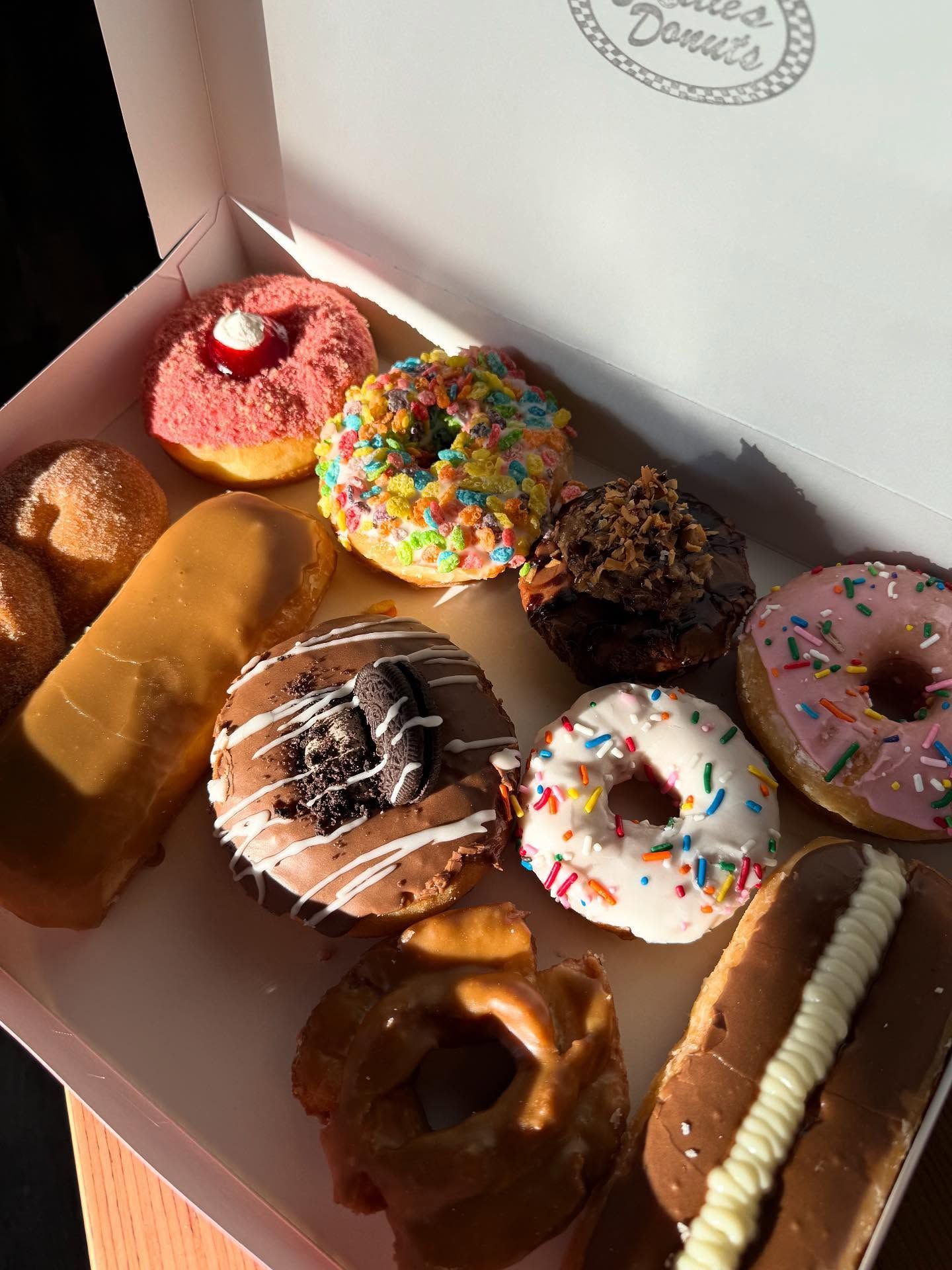 Box of colorful donuts with various toppings.