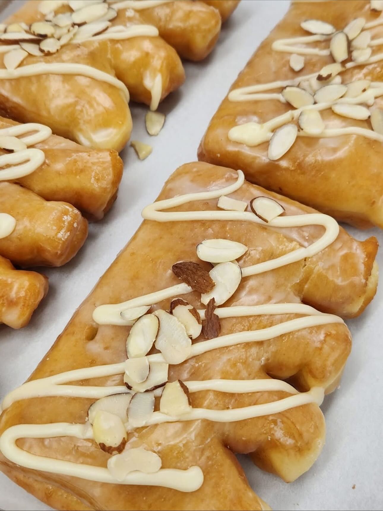 Glazed pastries shaped like trees, drizzled with white icing and topped with sliced almonds.