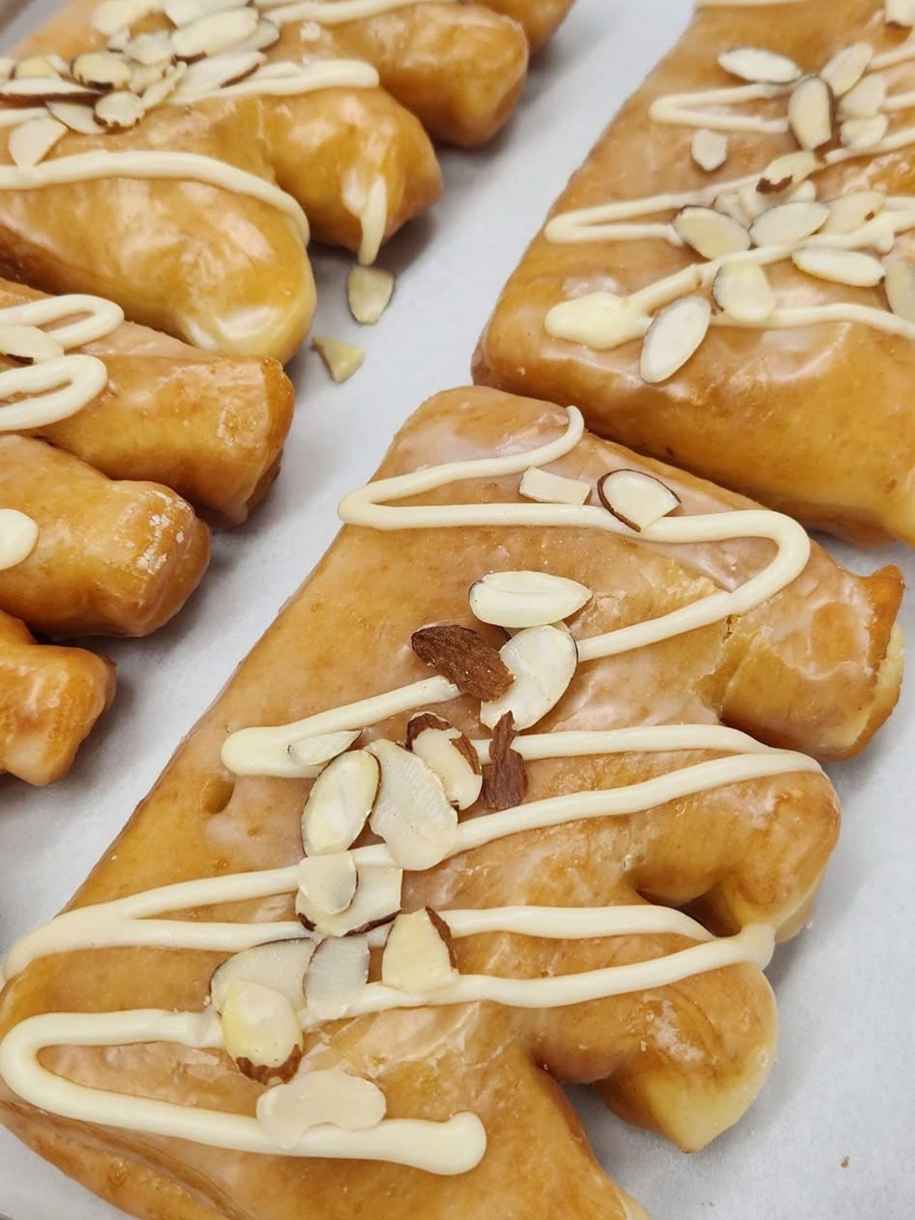 Glazed, tree-shaped pastries with white icing drizzle and almond slivers on a white surface.