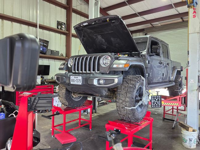 Black Jeep Wrangler on red hydraulic lifts in a garage with hood open, front end partially disassembled | Phase 2 Automotive