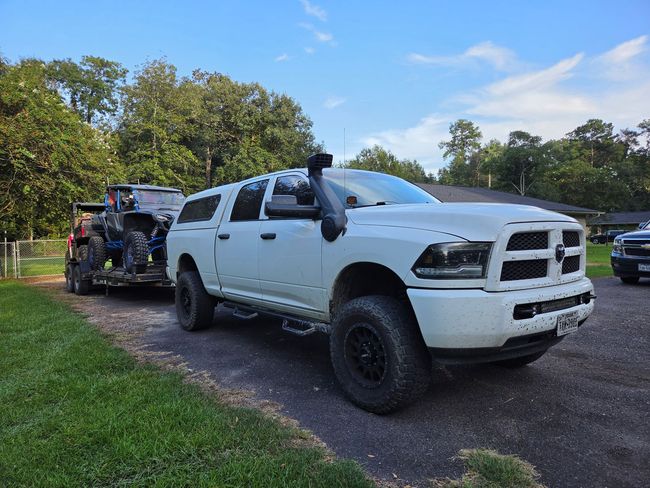 White lifted pickup truck towing a trailer on a gravel road beside a grassy park | Phase 2 Automotive