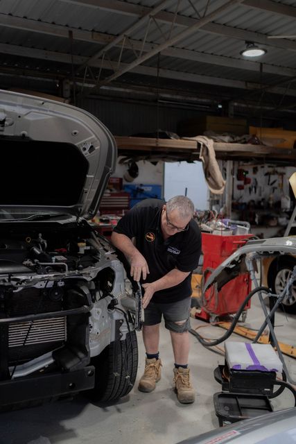 Mechanic working on a car in a workshop, using tools. Silver car, dark shirt, shorts — Douglas Collision Management In Currajong, QLD