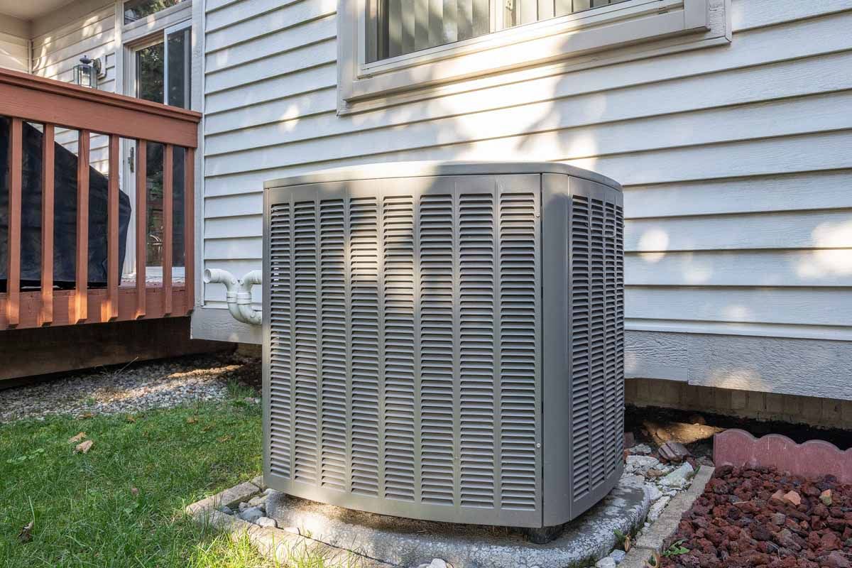 Air conditioning unit outside a white house, next to a wooden deck.