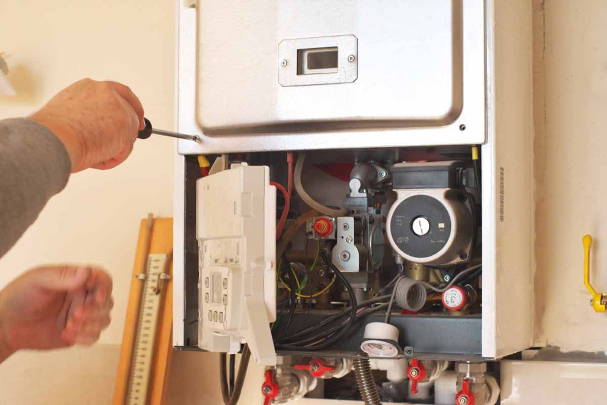 A person repairs a home heating unit using a screwdriver; setting is indoors.