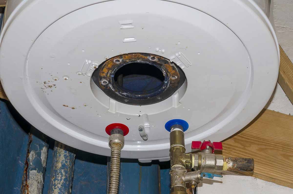 Close-up of a white water heater's top with rusty metal and water inlet/outlet pipes.