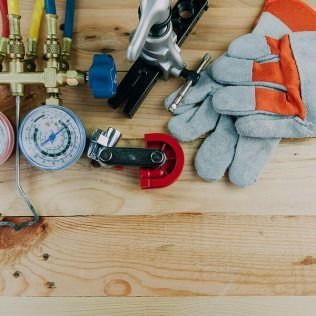 HVAC tools including gauges, gloves, and a pipe bender on a wooden surface.