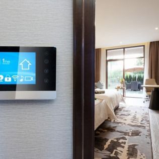 Smart home control panel on wall, view into bedroom with patio doors.