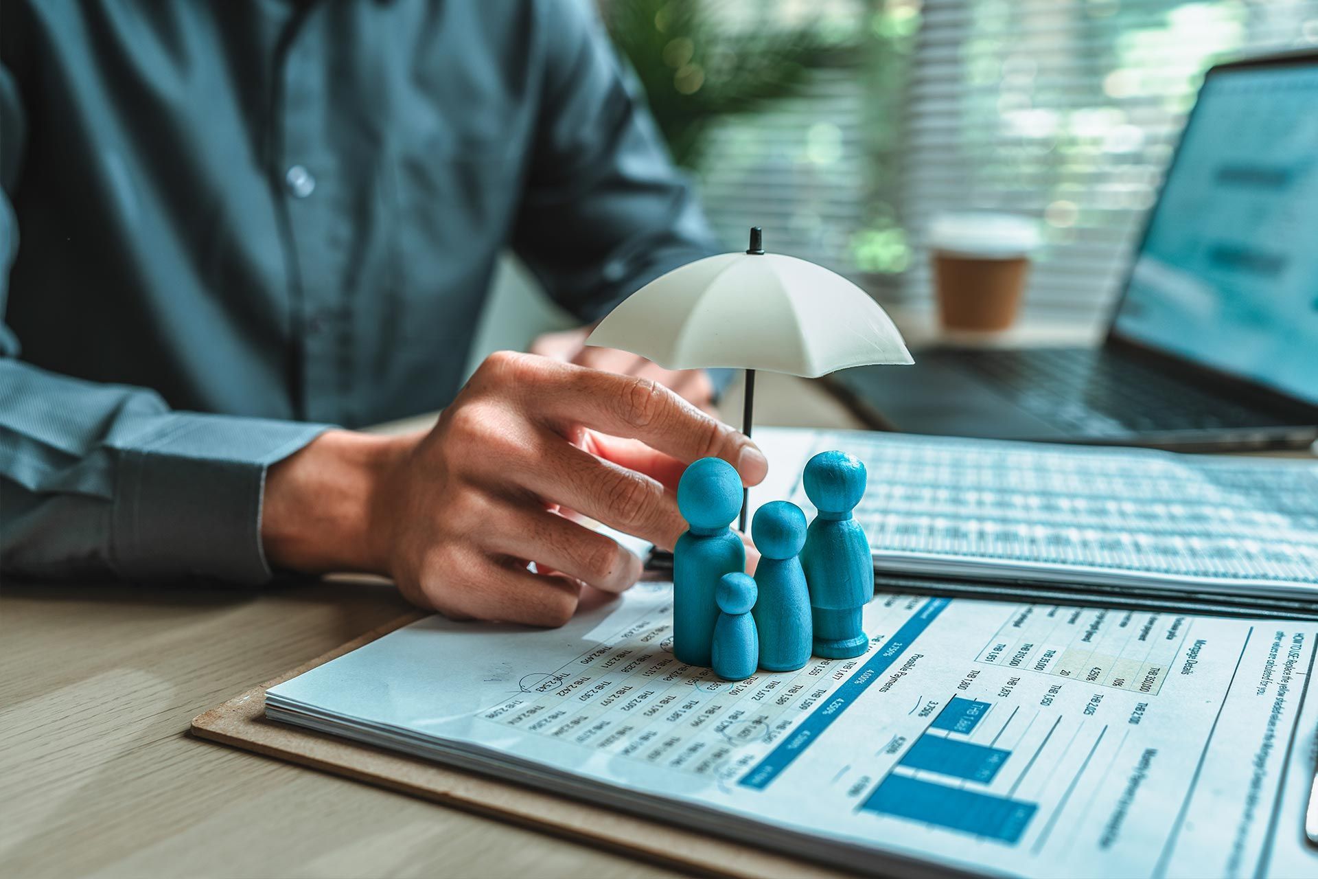 Person protecting family figurines with a miniature umbrella; financial documents in the background.