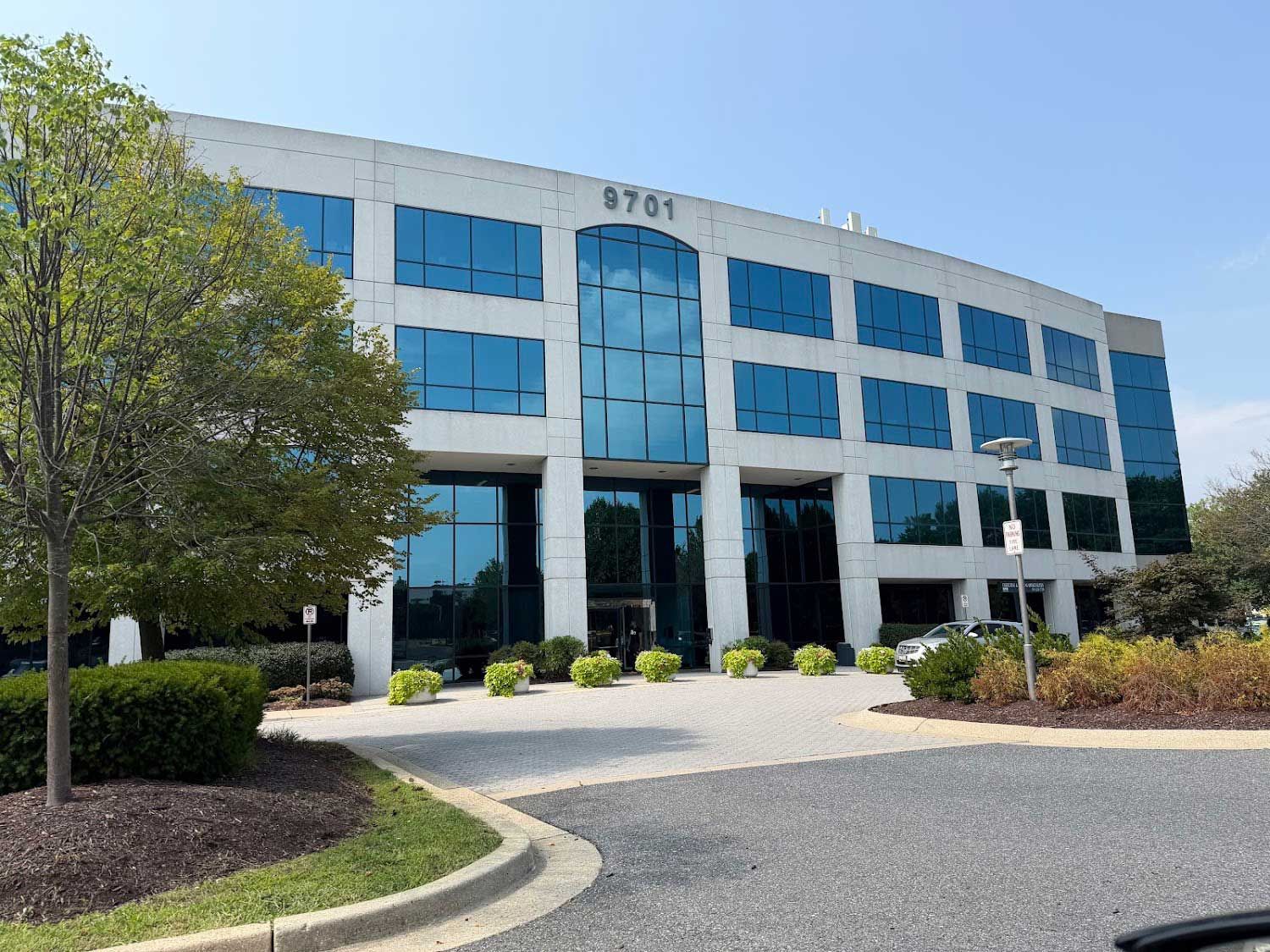 Modern office building with blue windows, white facade, and landscaped entrance under a clear sky