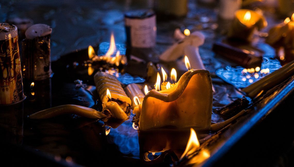 Altar encendido con velas y flores; persona ofrece alimentos en rito de memoria de los difuntos