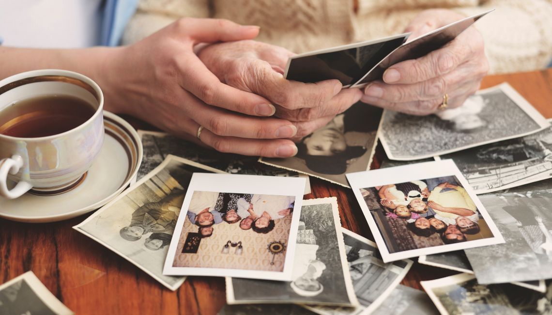 Manos de una persona mayor y una persona más joven revisando fotografías familiares antiguas sobre una mesa.