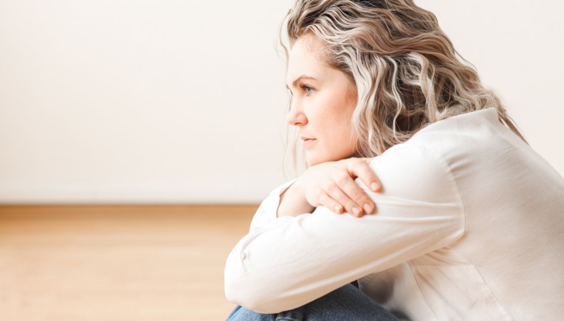 Mujer sentada en silencio reflexionando sobre el duelo por una madre ausente.