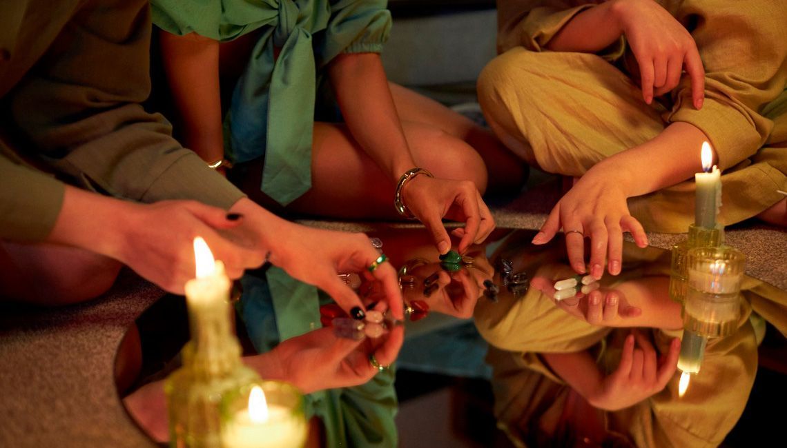 Personas realizando un ritual espiritual con velas y piedras sobre un espejo, en un ambiente íntimo y reflexivo.