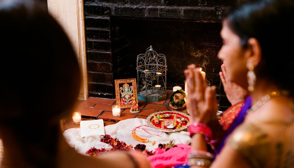 Mujer hindú con sari rojo en un acto de oración, con las manos juntas y rodeada de velas encendidas, en un ambiente de devoción.