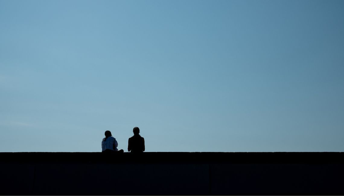 Dos personas sentadas en silencio, en silueta, bajo un cielo amplio; imagen sobre duelo y relaciones que cambian.