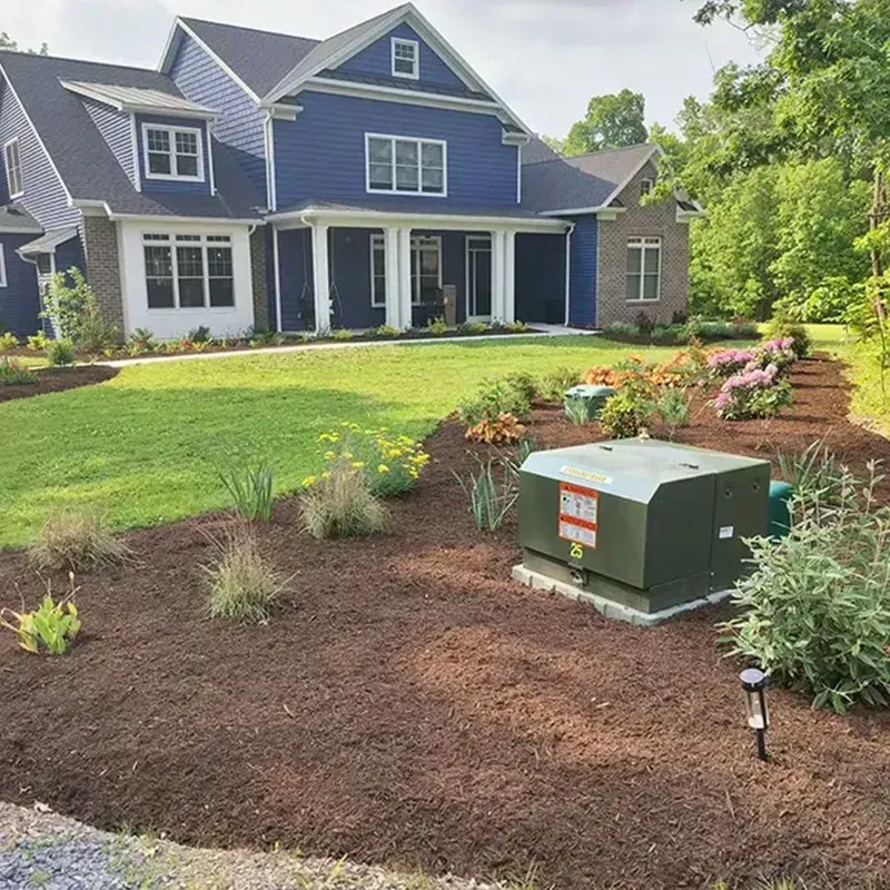 Blue house with white trim and a landscaped front yard featuring mulch, flowers, and a utility box