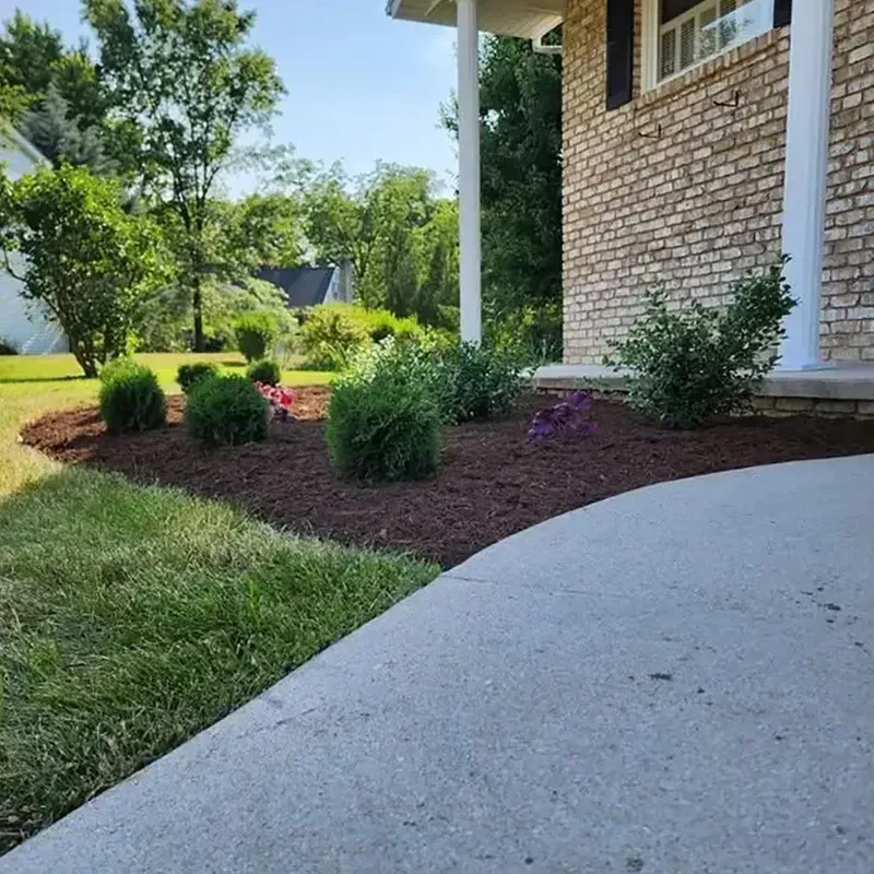 Front yard garden with shrubs and flowers beside a brick house and curved concrete walkway