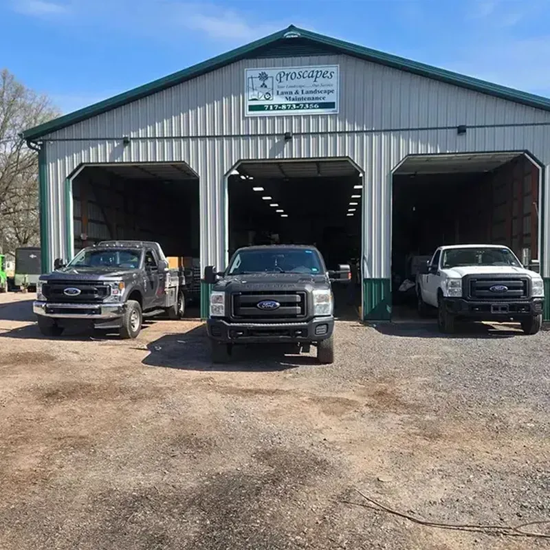 Three pickup trucks parked in front of a metal garage with open bays.