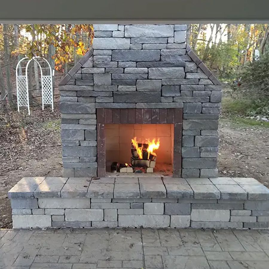 Stone outdoor fireplace with a lit fire in a backyard patio area