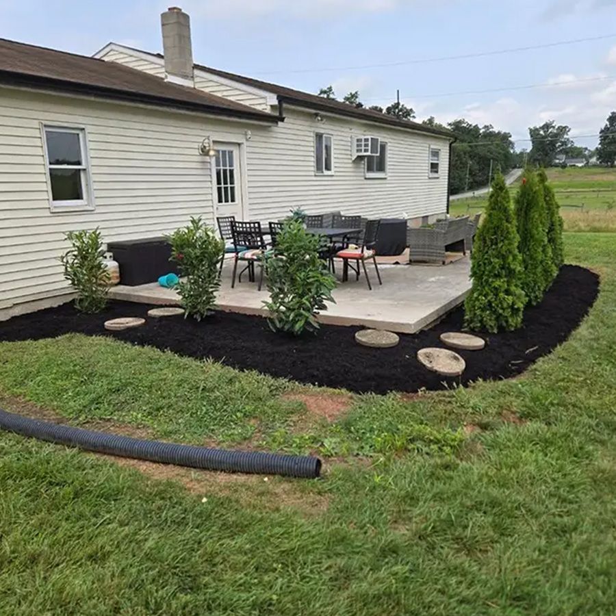 Backyard patio with outdoor seating, black mulch landscaping, and stepping stones beside a house