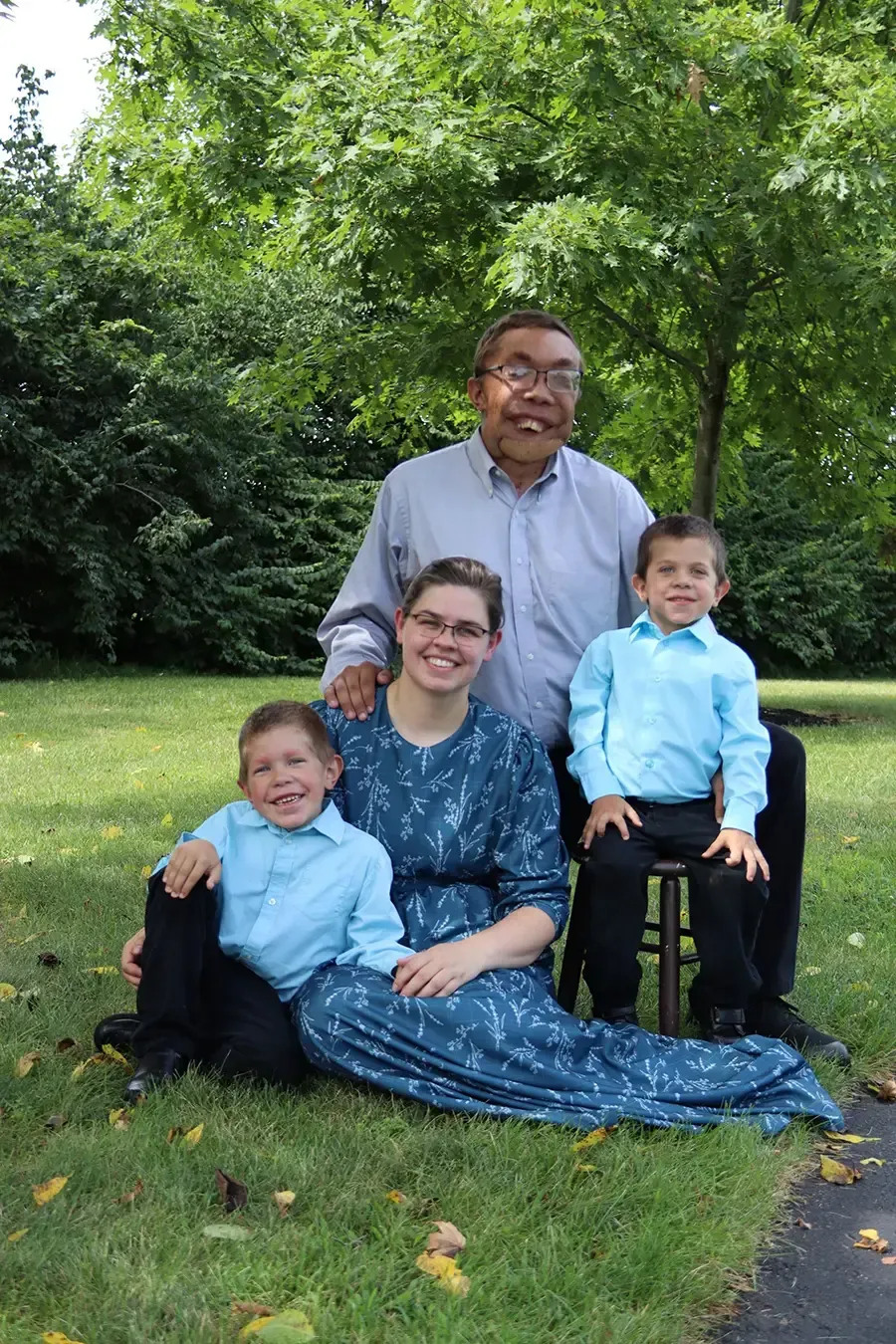 Four people sitting on grass in a park, with trees in the background.