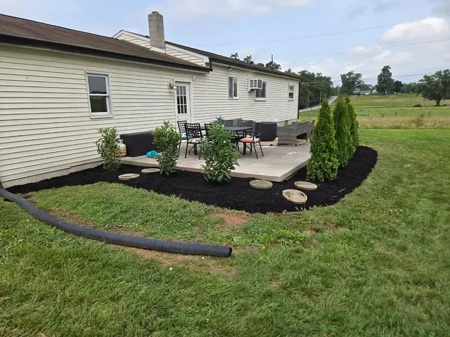 Backyard patio with outdoor furniture, potted plants, and a cream-colored house beside a grassy yard