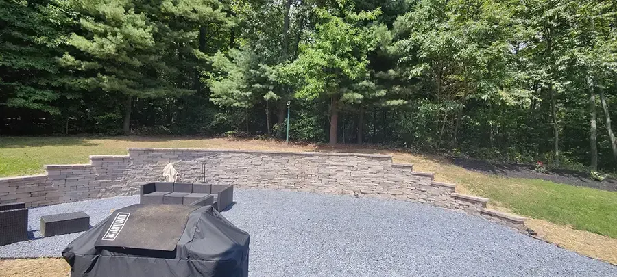 Gravel fire pit area with curved stone seating and trees in the background