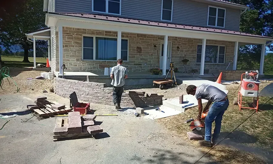 Workers building a house porch, with tools and materials scattered in a sunny yard.