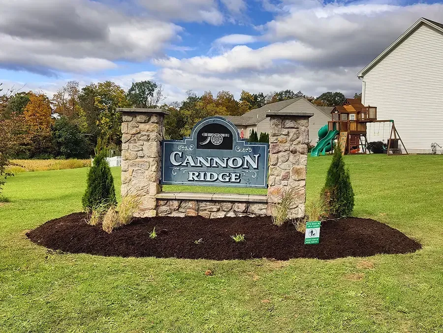 Stone sign for Cannon Ridge in a landscaped yard with a white house in the background.