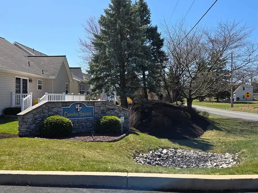 Stone entrance sign and landscaped lawn in front of a beige building on a sunny day
