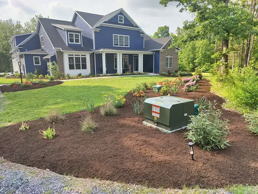 Large blue house with a landscaped front yard and a green utility box in a mulched garden bed.