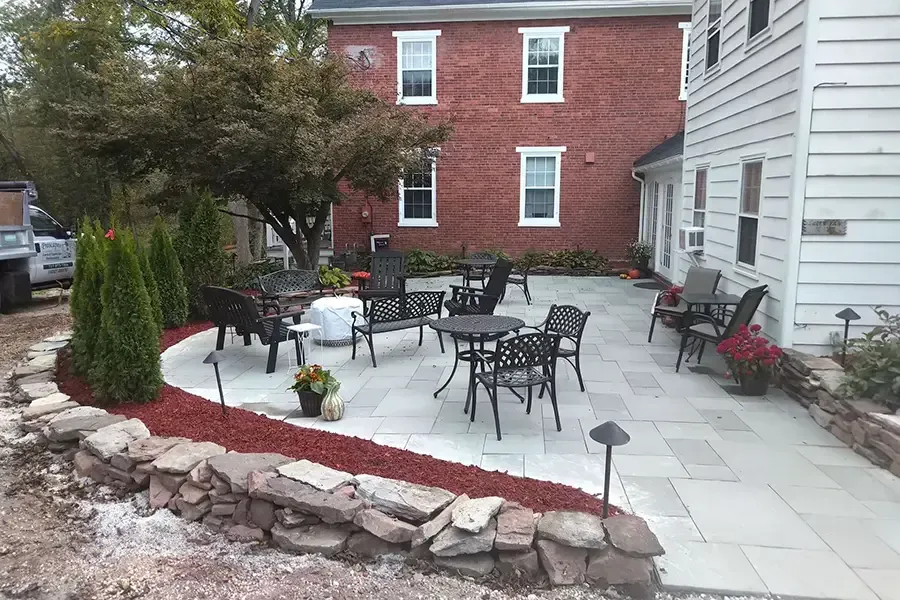 Small patio with black metal tables and chairs beside a red brick building and white house wall