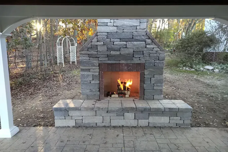 Stone outdoor fireplace with a burning fire under a covered patio
