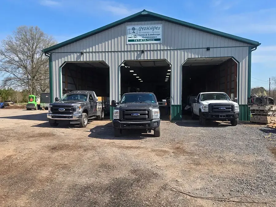 Three trucks parked outside a metal garage with open bays on a gravel lot.