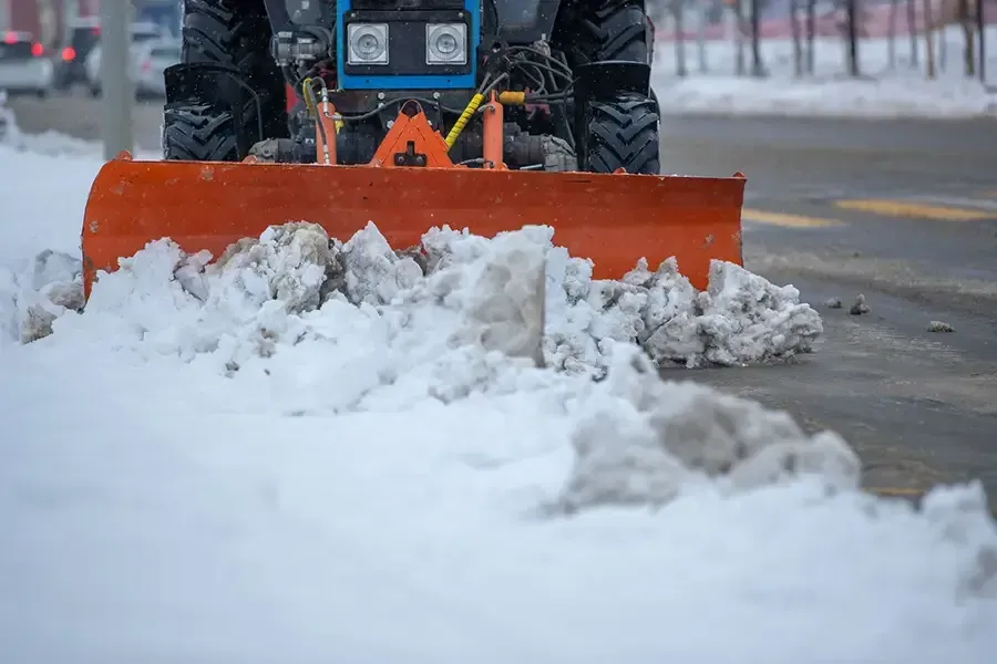 Orange snowplow clearing snow on a street, pushing a pile of snow forward