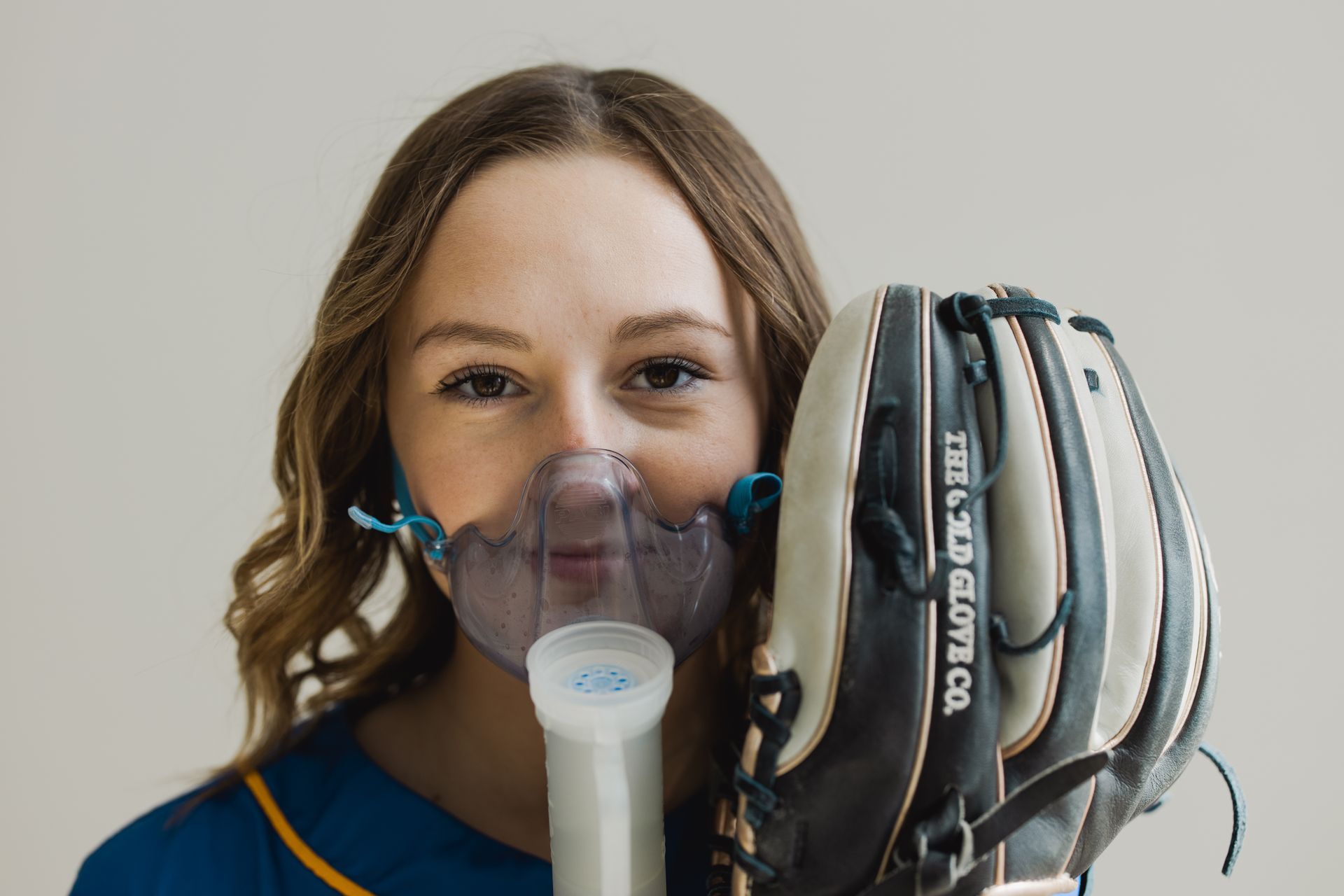 A girl with cystic fibrosis wearing a breathing mask and holding a baseball mitt