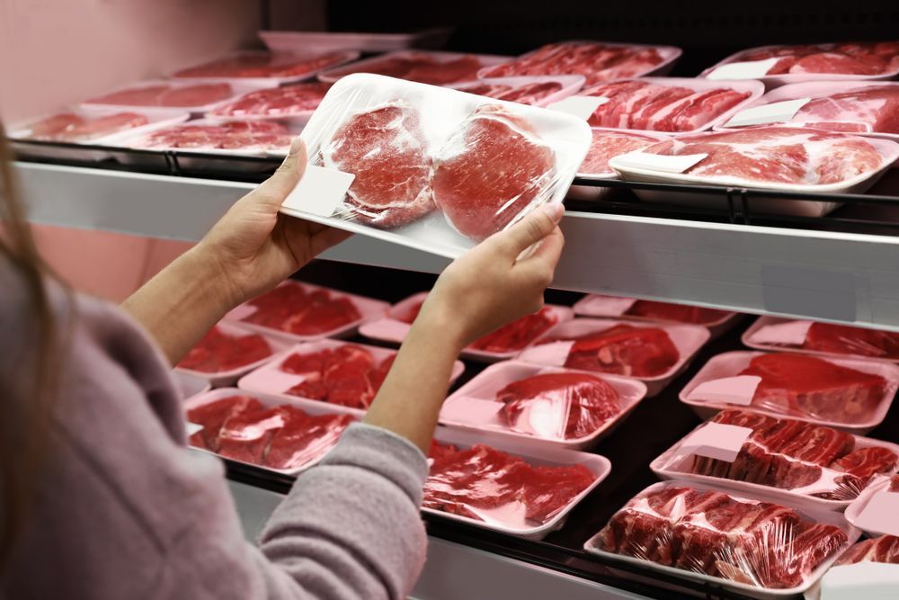 Woman taking packed pork meat from shelf — Wholesale Butchery in Cobar, NSW