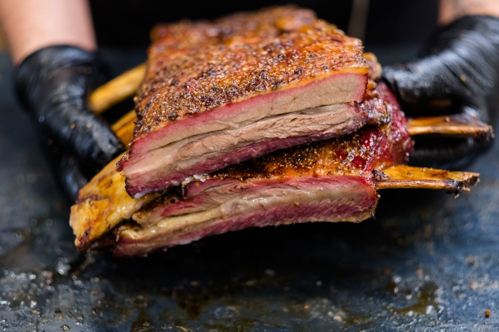 Chef hands in black cooking gloves holding smoked beef ribs — Wholesale Butchery in Nyngan, NSW