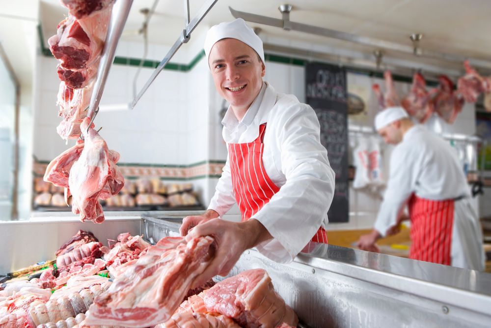 Butcher smiling and holding meat — Wholesale Butchery in Walgett, NSW