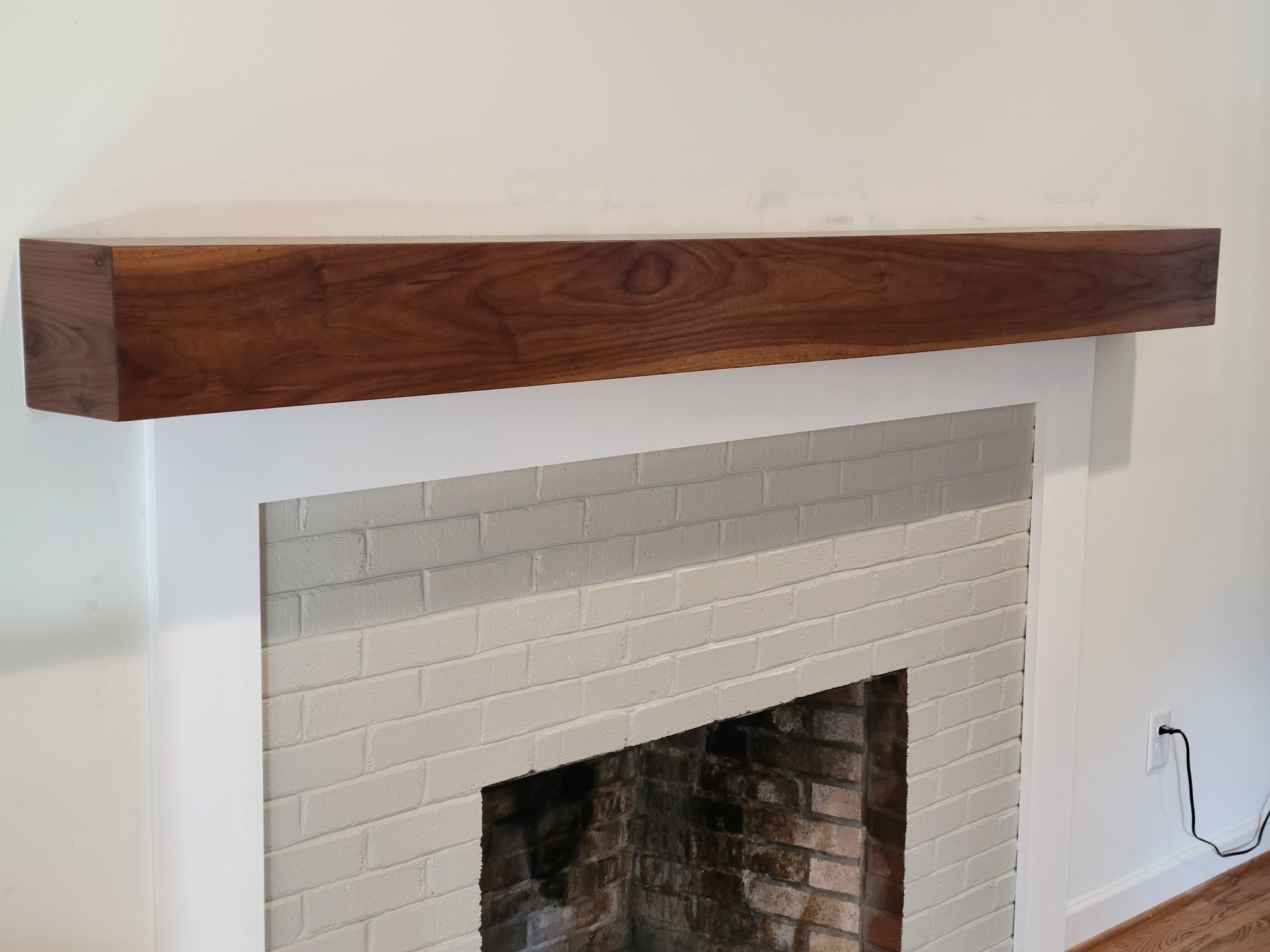 A white brick fireplace with a wooden mantle above it.