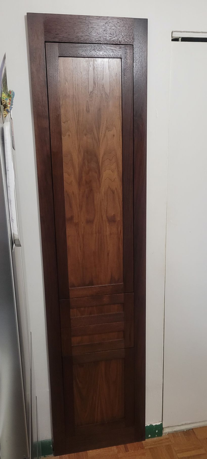 A wooden door is sitting in a room next to a white wall.