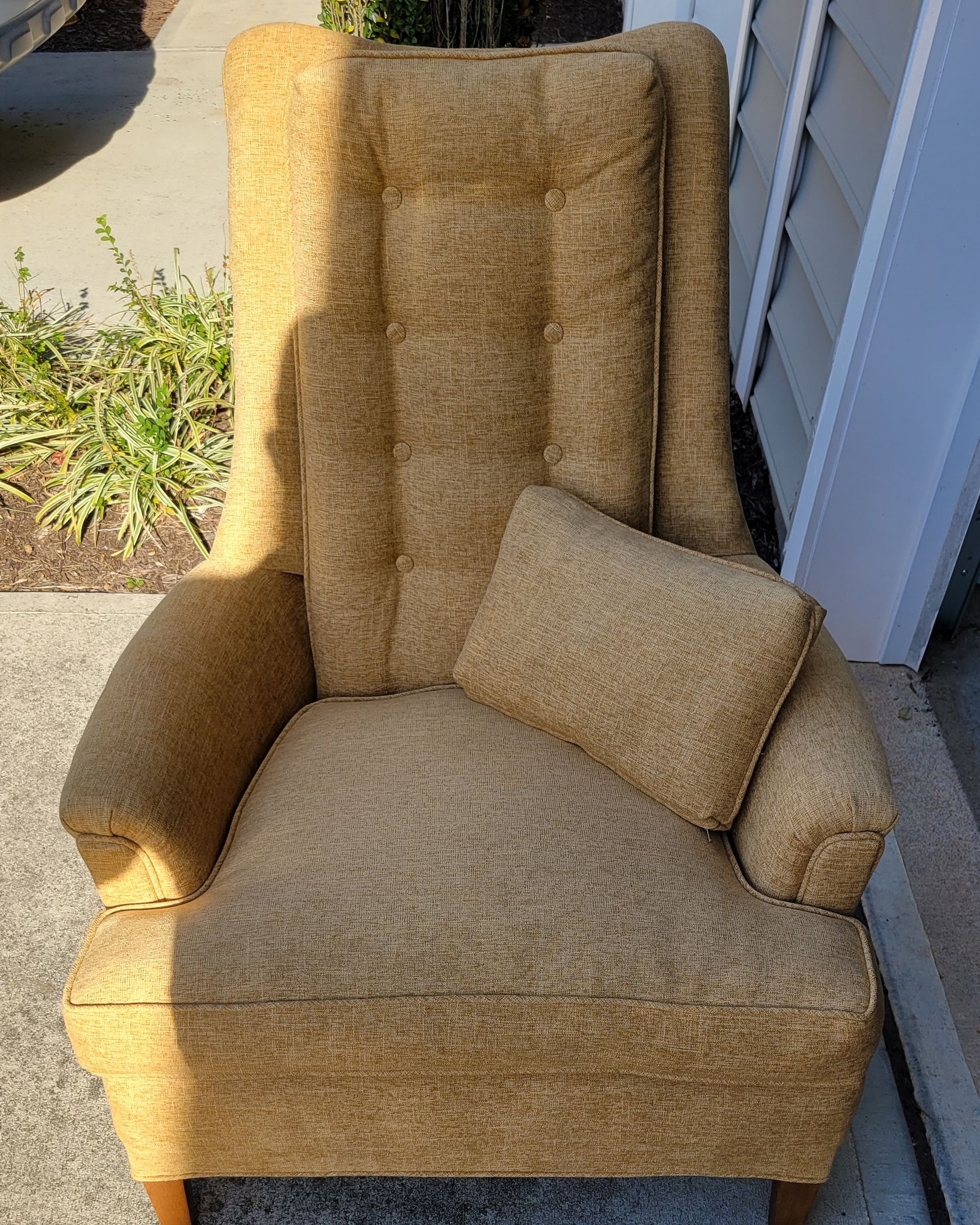 A chair with a pillow on it is sitting on a sidewalk next to a house.