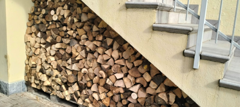 Legna da ardere accatastata sotto le scale esterne accanto a un muro giallo