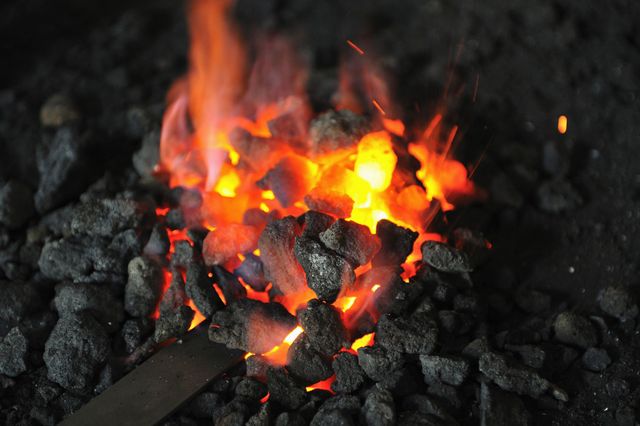 Fiamme arancioni incandescenti tra pezzi di carbone nero in un braciere buio