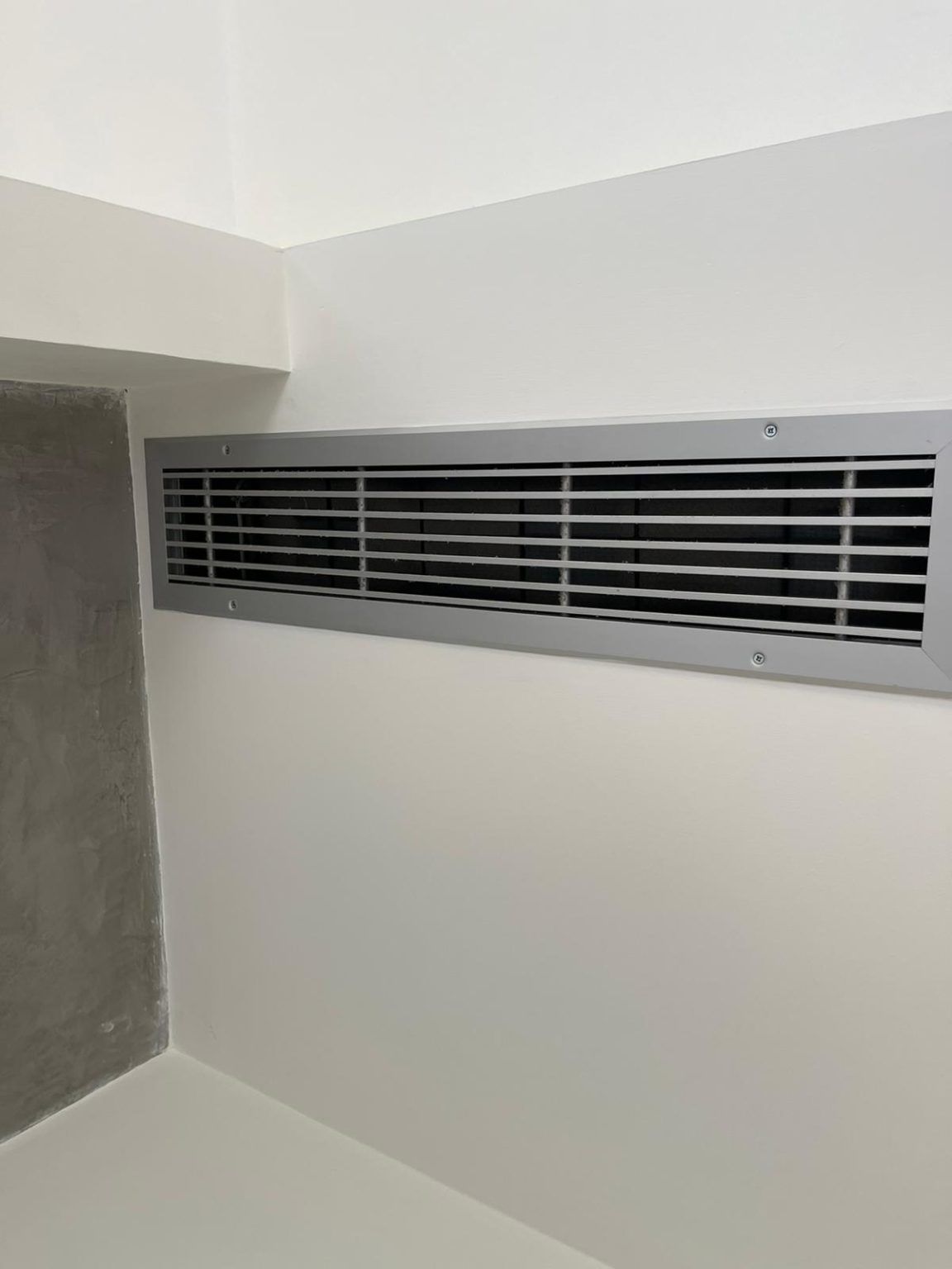 A white wall with a metal grille on it.