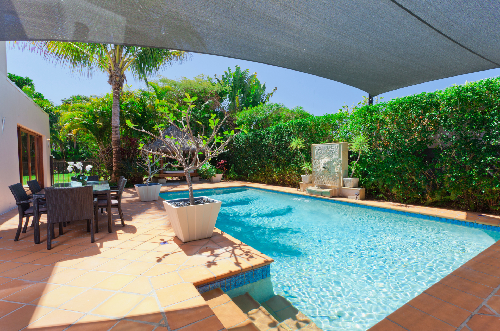 A straw hat , a book , and a drink are sitting next to a swimming pool.