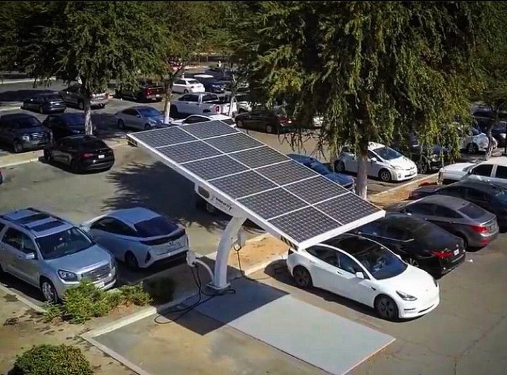 Una marquesina solar cubre los coches aparcados en un estacionamiento, con varios vehículos blancos y azules debajo.